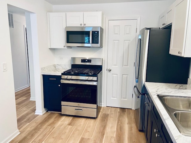 kitchen featuring light stone counters, visible vents, stainless steel appliances, light wood-style floors, and white cabinetry