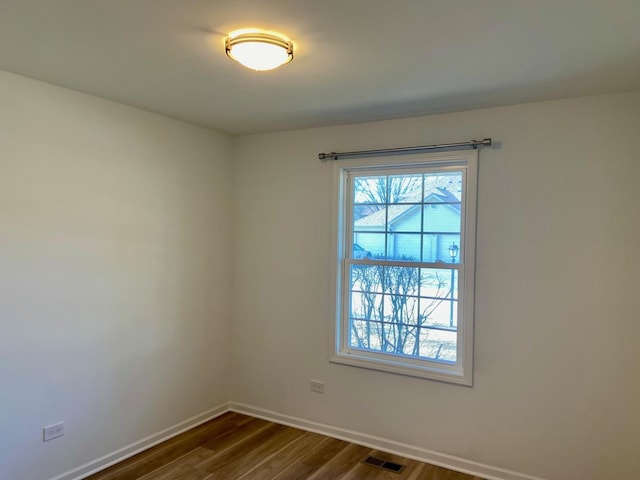 spare room with dark wood-style floors, visible vents, and baseboards