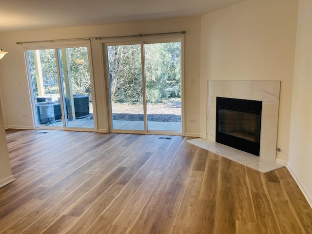 unfurnished living room featuring wood finished floors, visible vents, a high end fireplace, and baseboards