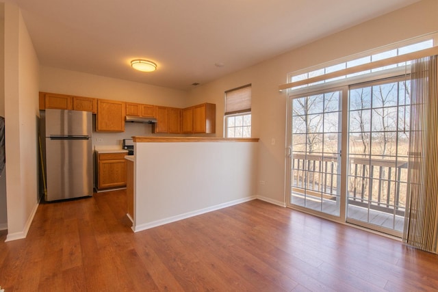 kitchen featuring under cabinet range hood, freestanding refrigerator, baseboards, and dark wood-style flooring