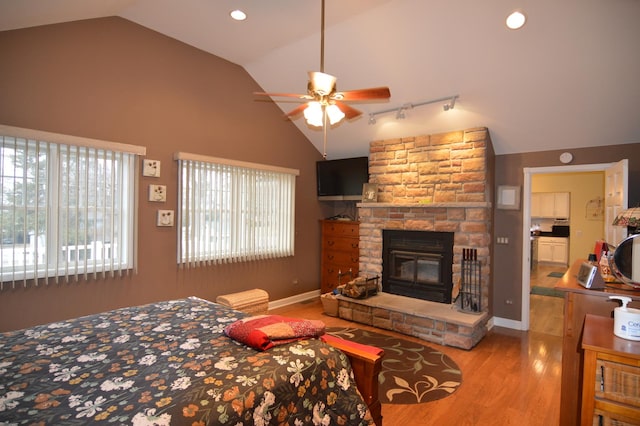 bedroom featuring lofted ceiling, wood finished floors, recessed lighting, a stone fireplace, and baseboards