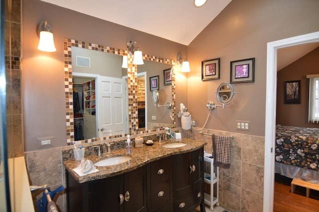 full bath with vaulted ceiling, connected bathroom, tile walls, and a sink