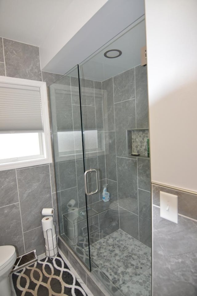 bathroom with a shower stall, toilet, tile walls, and visible vents