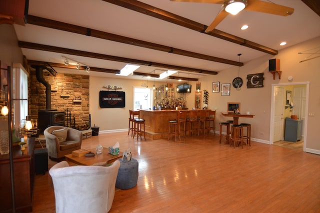 living area with beam ceiling, a wood stove, wood finished floors, and baseboards