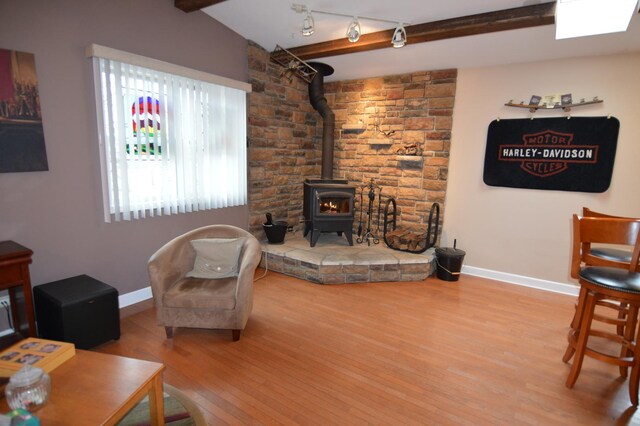 living room with beamed ceiling, baseboards, wood finished floors, and a wood stove