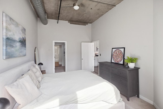 bedroom with light colored carpet, connected bathroom, a high ceiling, and baseboards