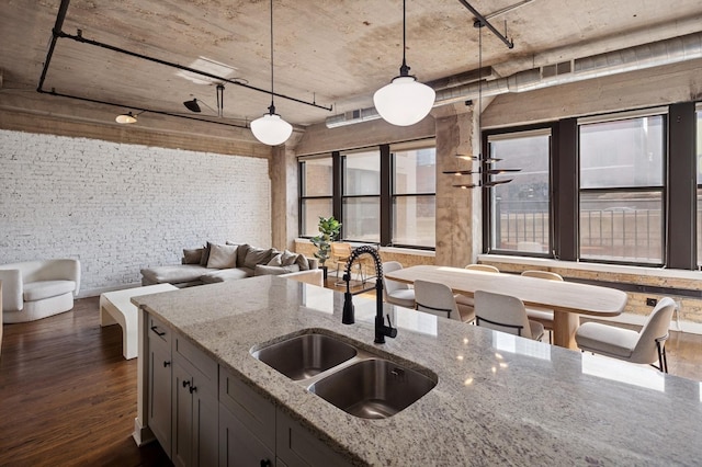 kitchen featuring light stone counters, brick wall, a sink, dark wood-type flooring, and pendant lighting