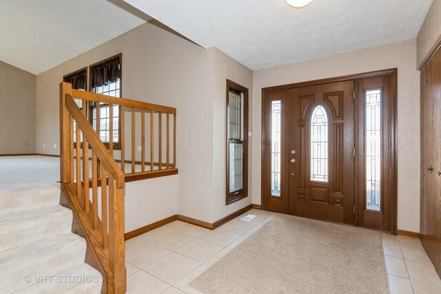 entrance foyer featuring light tile patterned flooring, light carpet, stairs, and baseboards