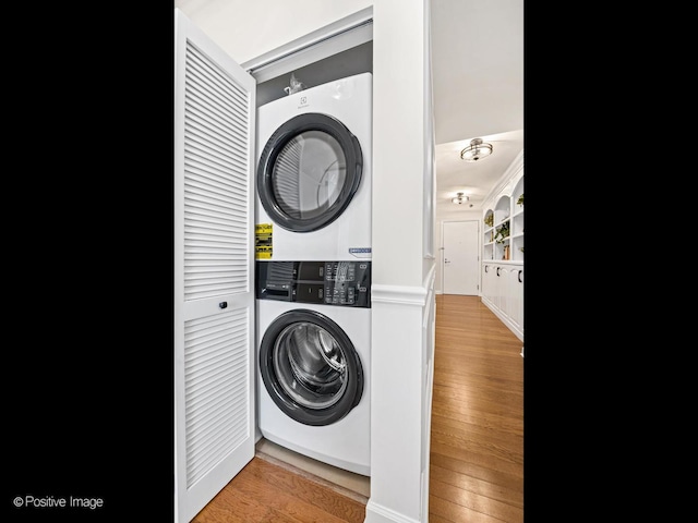 laundry room with stacked washer and clothes dryer, wood finished floors, and laundry area