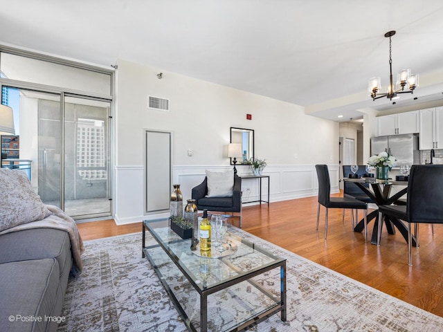 living room with visible vents, a wainscoted wall, an inviting chandelier, and wood finished floors