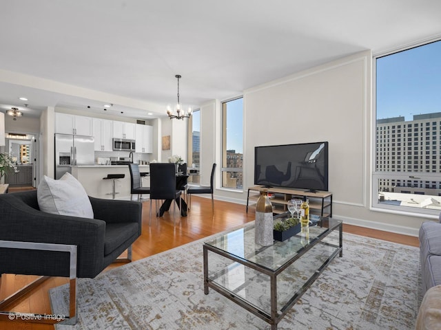 living room featuring an inviting chandelier, plenty of natural light, baseboards, and light wood finished floors