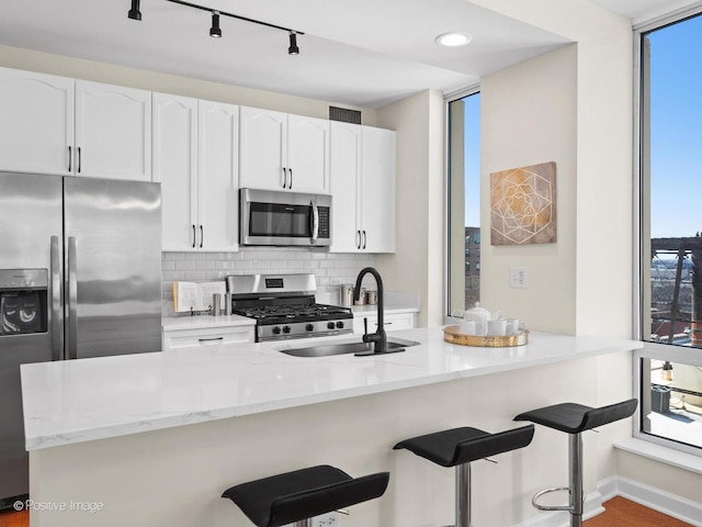 kitchen featuring light stone countertops, a sink, decorative backsplash, white cabinets, and appliances with stainless steel finishes