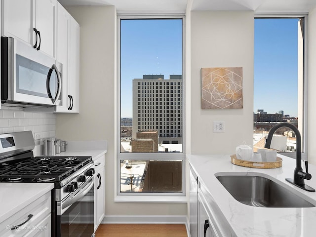 kitchen with white cabinetry, a sink, appliances with stainless steel finishes, a city view, and backsplash