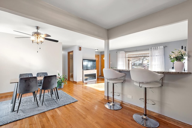 dining space with ceiling fan, light wood-style flooring, baseboards, and a tile fireplace