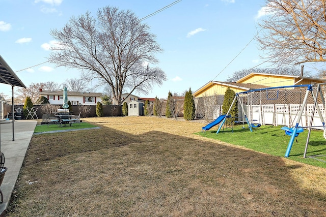 view of yard with a playground, a fenced backyard, an outdoor structure, a patio area, and a storage unit