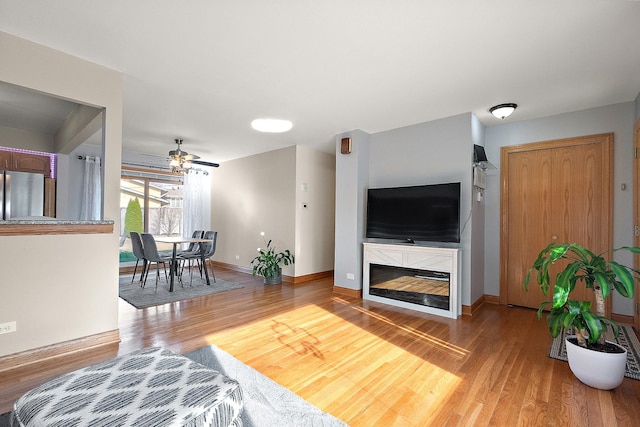 living area featuring a glass covered fireplace, baseboards, and light wood-style floors