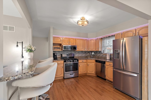 kitchen featuring visible vents, dark stone countertops, backsplash, wood finished floors, and stainless steel appliances