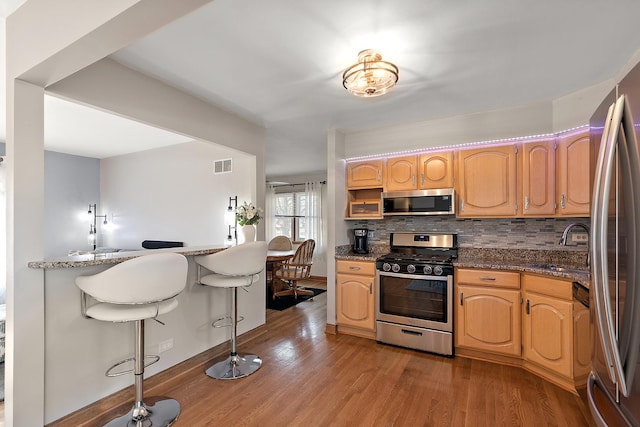 kitchen featuring visible vents, a kitchen breakfast bar, wood finished floors, stainless steel appliances, and a sink