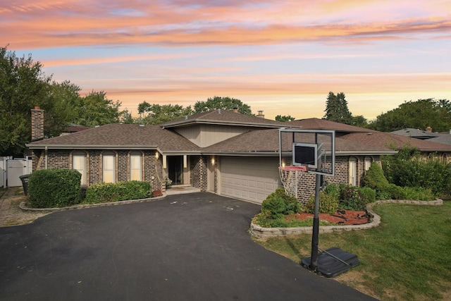 prairie-style house featuring a lawn, aphalt driveway, an attached garage, brick siding, and a chimney