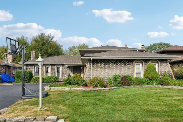 view of front of home with a shingled roof, a front yard, brick siding, and a chimney