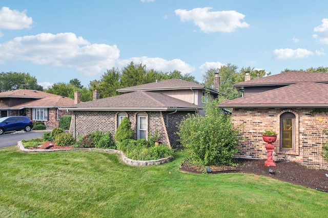 view of front of property featuring a front yard, brick siding, a chimney, and a shingled roof