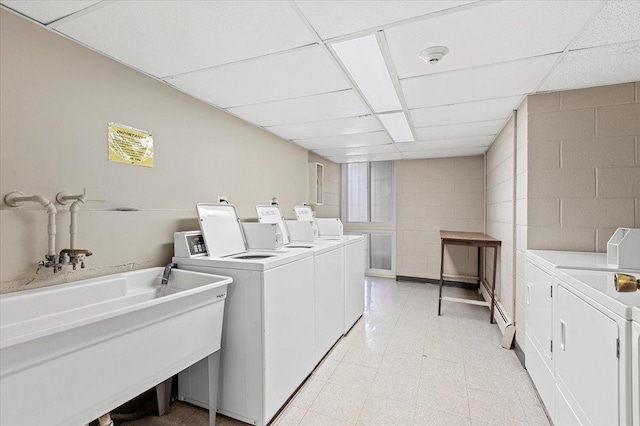 common laundry area featuring a sink, separate washer and dryer, light floors, and concrete block wall