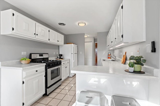 kitchen featuring visible vents, stainless steel gas stove, a sink, freestanding refrigerator, and light tile patterned floors