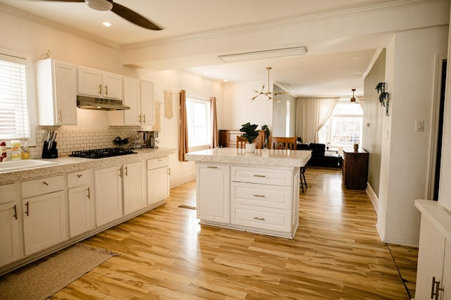 kitchen featuring under cabinet range hood, light wood-style flooring, black gas cooktop, and crown molding