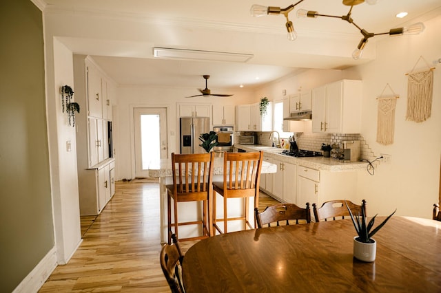 dining room featuring light wood finished floors, baseboards, a ceiling fan, and ornamental molding