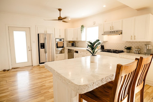 kitchen featuring under cabinet range hood, a wealth of natural light, a breakfast bar area, and appliances with stainless steel finishes