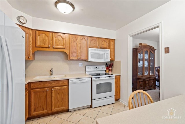 kitchen with brown cabinetry, white appliances, light countertops, and a sink