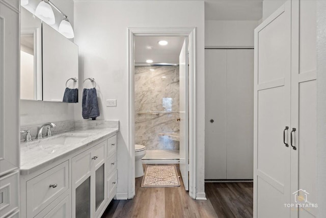 bathroom featuring wood finished floors, toilet, a stall shower, and vanity