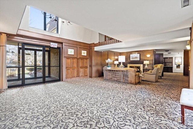 living area with visible vents, wooden walls, a warm lit fireplace, and a towering ceiling