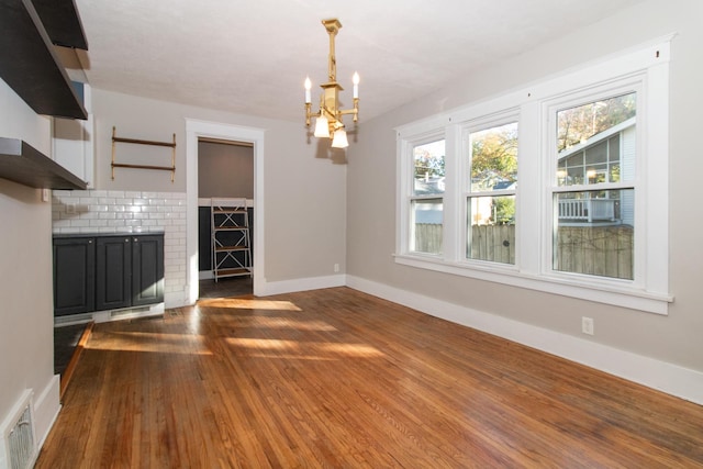 unfurnished living room featuring dark wood-style floors, visible vents, a notable chandelier, and baseboards