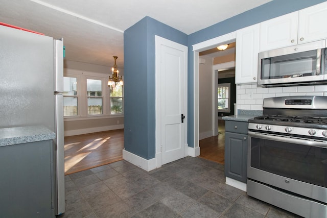 kitchen with backsplash, baseboards, appliances with stainless steel finishes, a notable chandelier, and white cabinetry