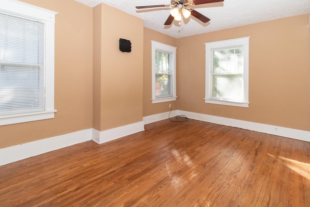 empty room with ceiling fan, wood finished floors, baseboards, and a textured ceiling