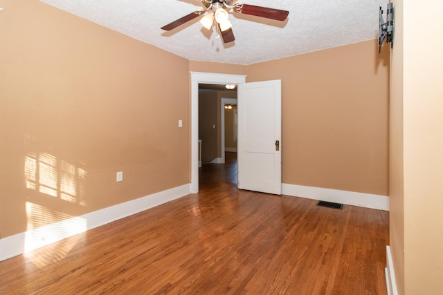 empty room with baseboards, wood finished floors, visible vents, and a textured ceiling