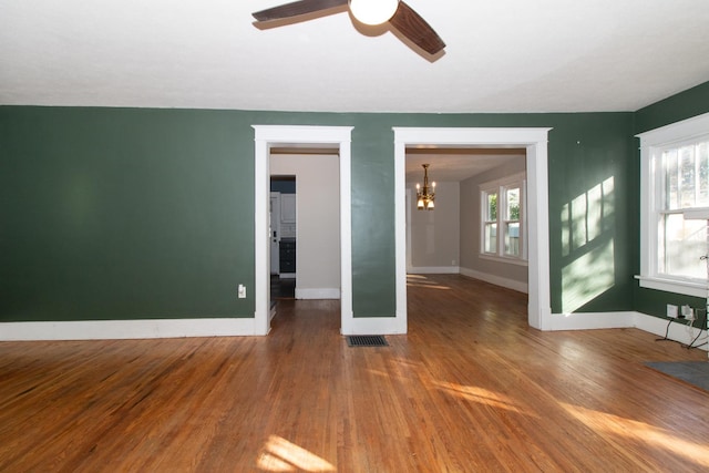 unfurnished room featuring visible vents, ceiling fan with notable chandelier, baseboards, and wood finished floors