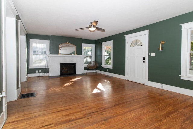 unfurnished living room with a brick fireplace, plenty of natural light, wood finished floors, and visible vents