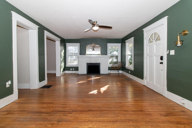 unfurnished living room featuring wood finished floors, a fireplace, visible vents, and ceiling fan