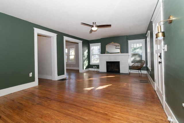 unfurnished living room featuring a brick fireplace, wood finished floors, baseboards, and a wealth of natural light