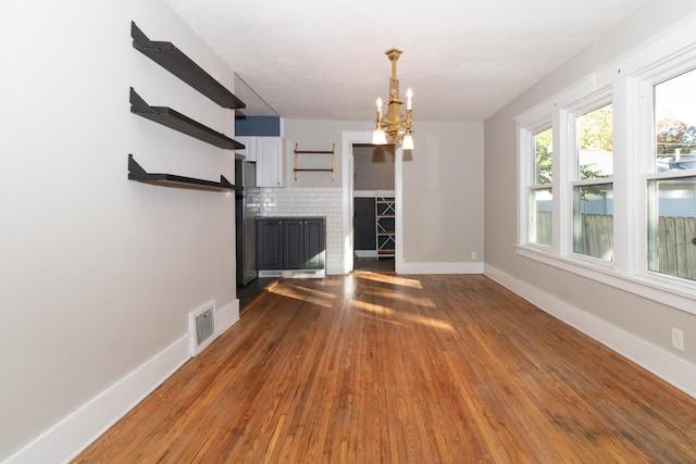 unfurnished living room with a chandelier, visible vents, baseboards, and wood finished floors