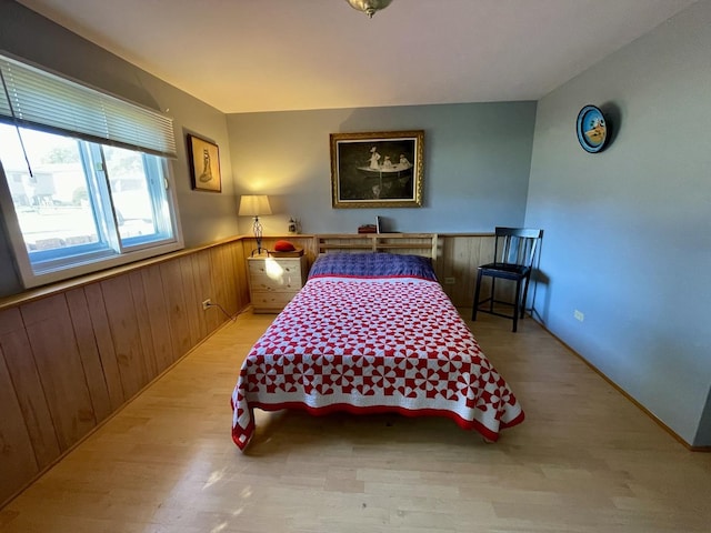 bedroom featuring light wood finished floors, wood walls, and wainscoting