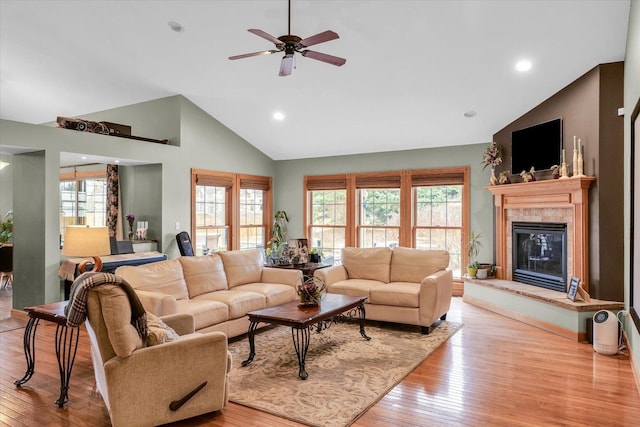 living room with a tiled fireplace, ceiling fan, light wood-type flooring, and high vaulted ceiling