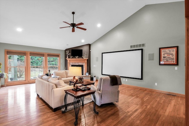 home theater featuring baseboards, visible vents, high vaulted ceiling, a fireplace, and wood-type flooring