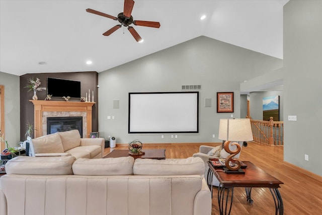 cinema room featuring light wood-type flooring, visible vents, a tiled fireplace, lofted ceiling, and ceiling fan