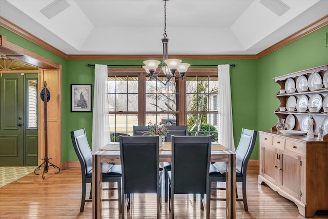 dining space with a notable chandelier, plenty of natural light, a raised ceiling, and light wood-style floors