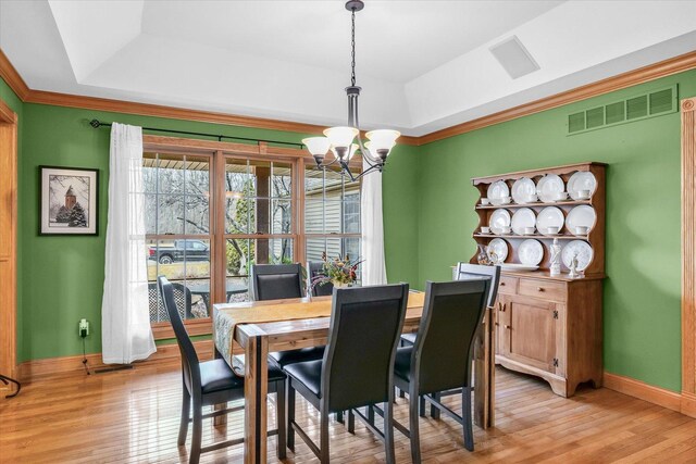 dining space with an inviting chandelier, a tray ceiling, visible vents, and light wood finished floors