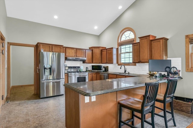 kitchen featuring a peninsula, a sink, stainless steel appliances, under cabinet range hood, and brown cabinets