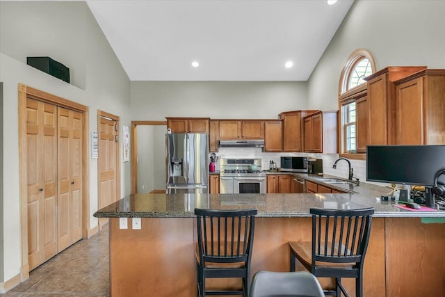 kitchen featuring high vaulted ceiling, a sink, stainless steel appliances, under cabinet range hood, and brown cabinets